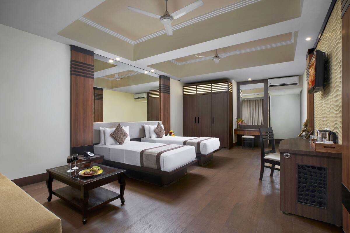 A hotel room with two beds, a desk, a chair, a coffee machine, and a TV.
