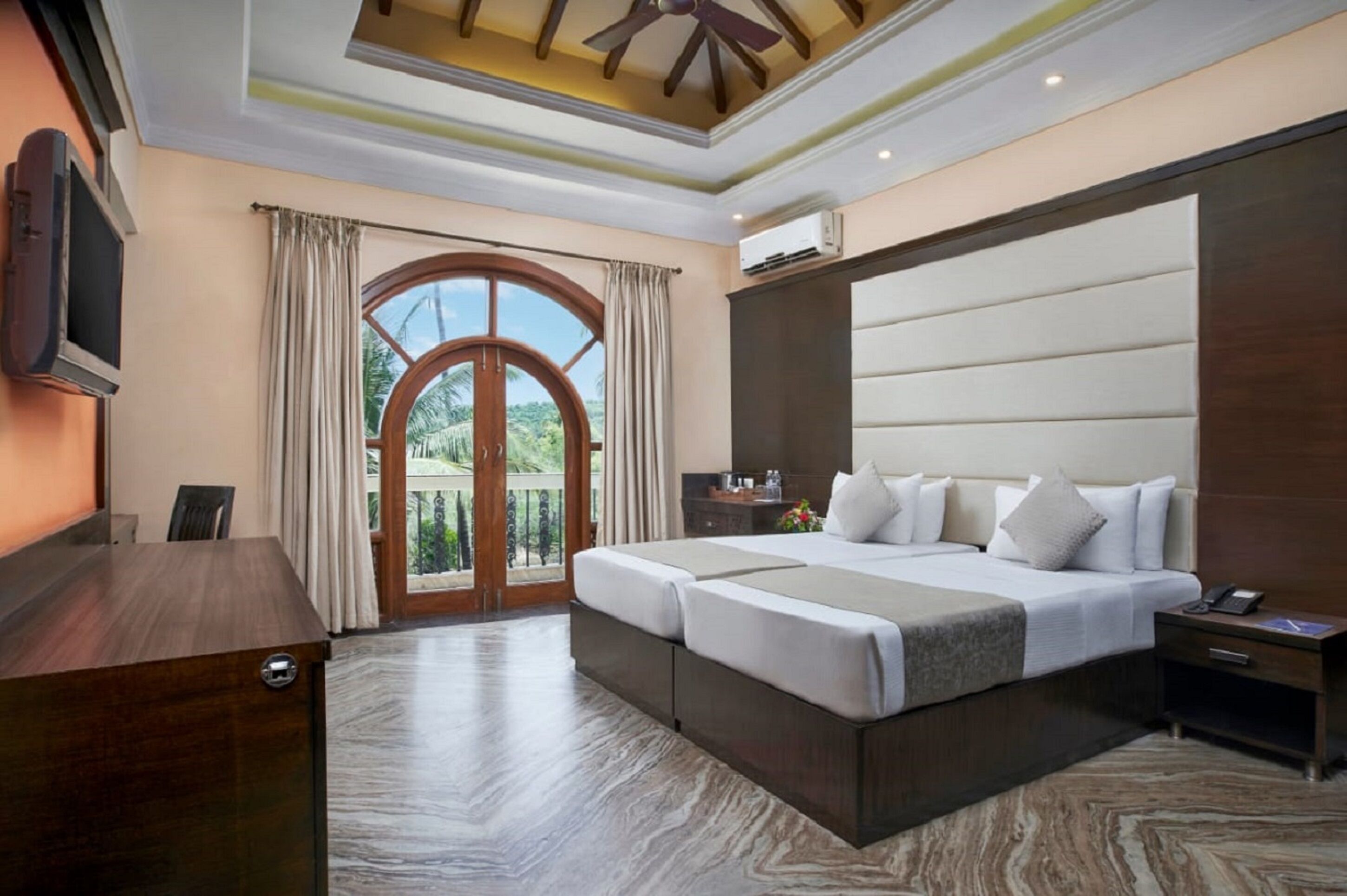 A hotel room with a large bed, a desk, a TV, and a balcony with curtains.