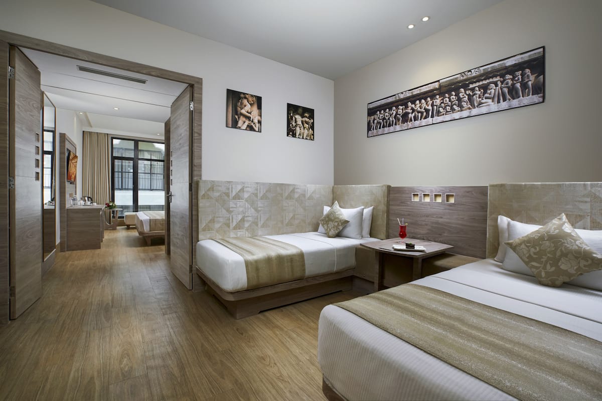 A hotel room with two beds, a large window, and artwork on the walls.