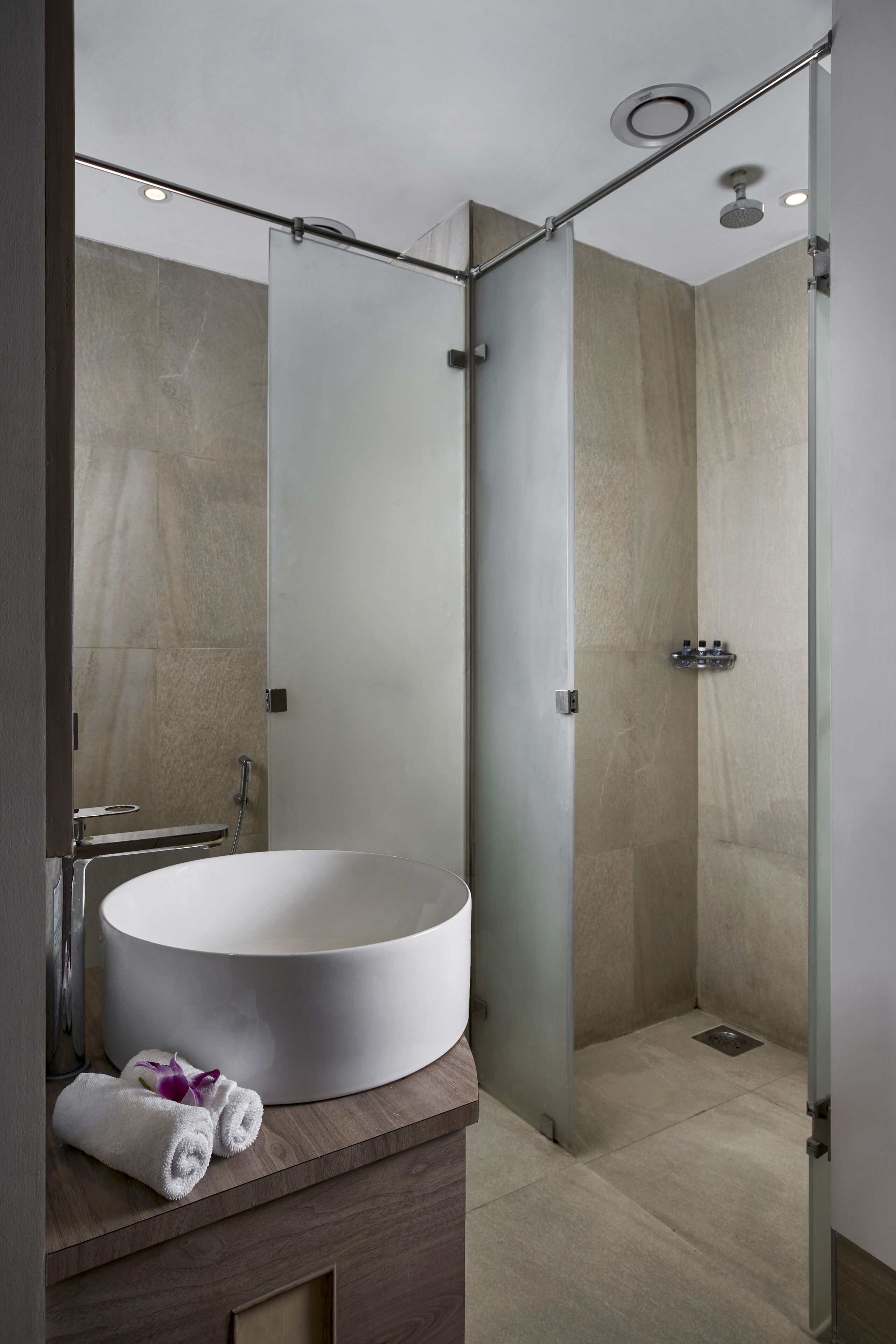 Un baño moderno con un lavamanos grande y redondo, una cabina de ducha con mampara de vidrio y un mueble de tocador de madera.