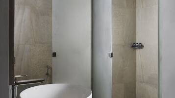 Un baño moderno con un lavamanos grande y redondo, una cabina de ducha con mampara de vidrio y un mueble de tocador de madera.