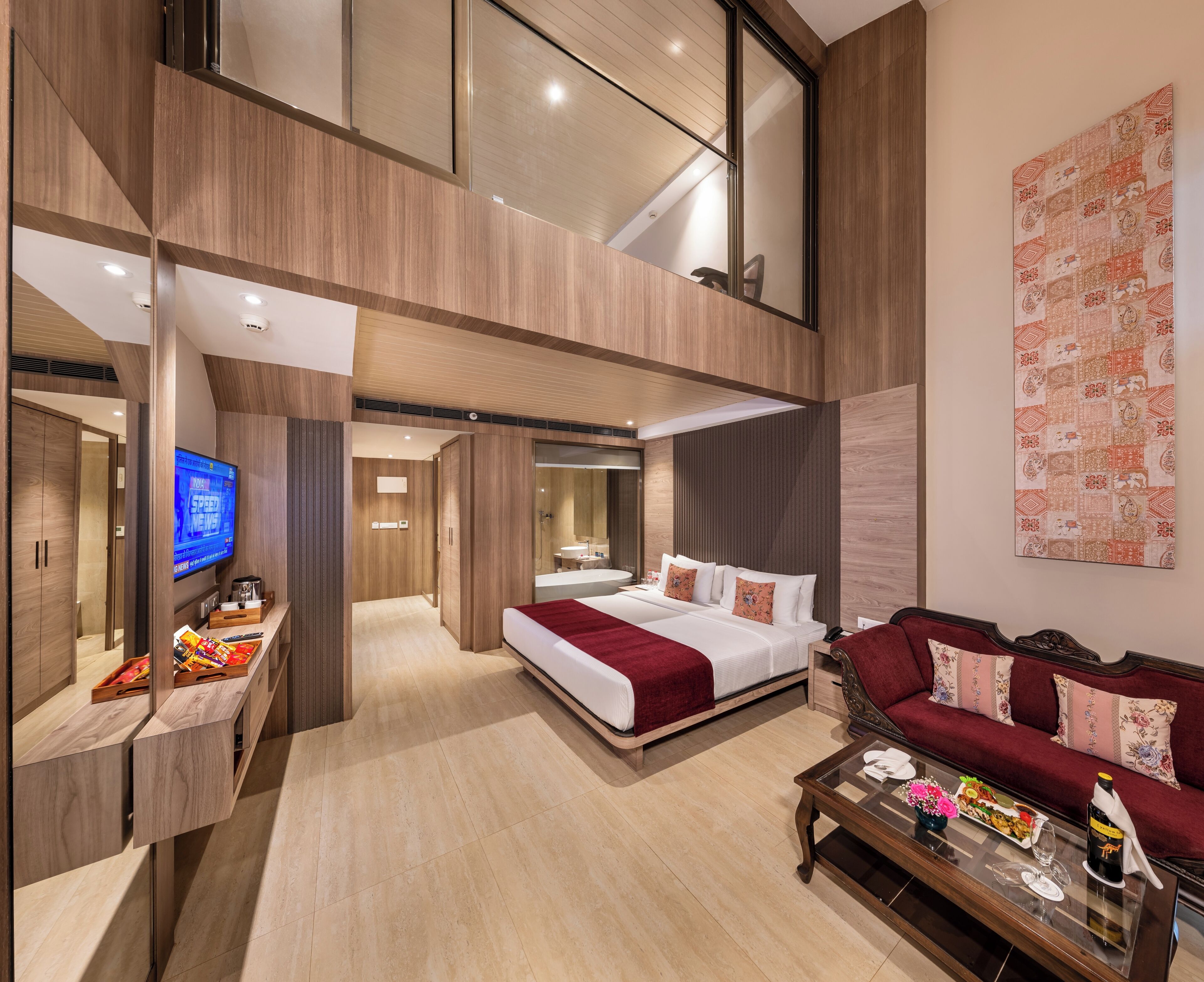 A modern hotel room with a large bed, a sofa, a TV, and a dining area.