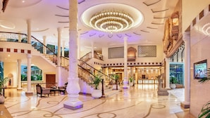 A grand lobby with a large chandelier, multiple staircases, and ornate columns.