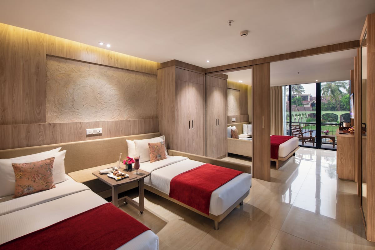 A modern hotel room with two beds, a small table with a drink, and a view of the outdoors.