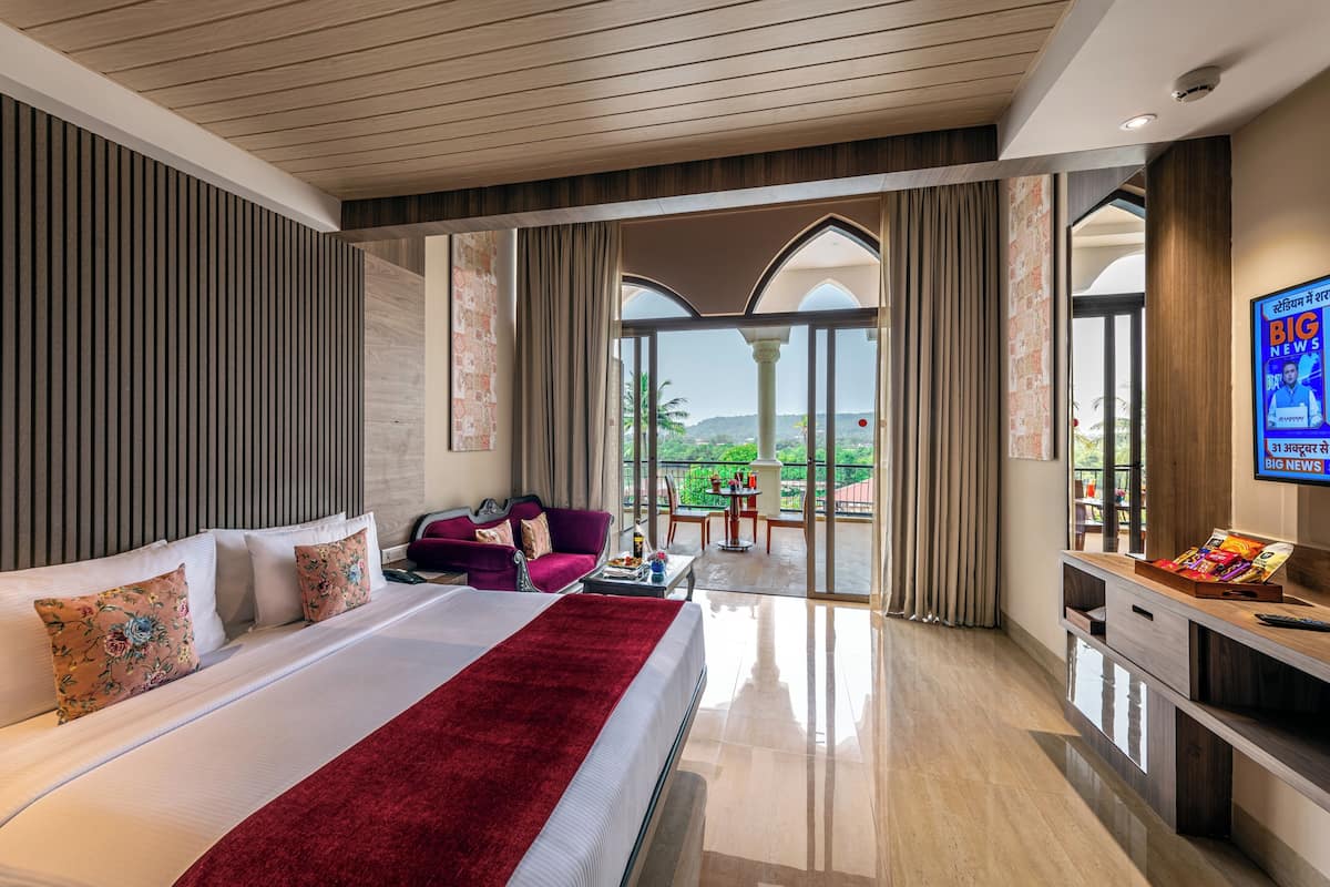 A modern hotel room with a large bed, a seating area, and a balcony with a view.