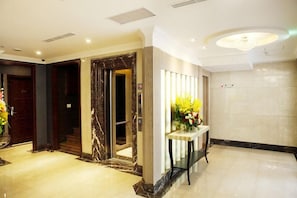 A hotel lobby with a marble reception desk, an elevator, and a wall-mounted sign.