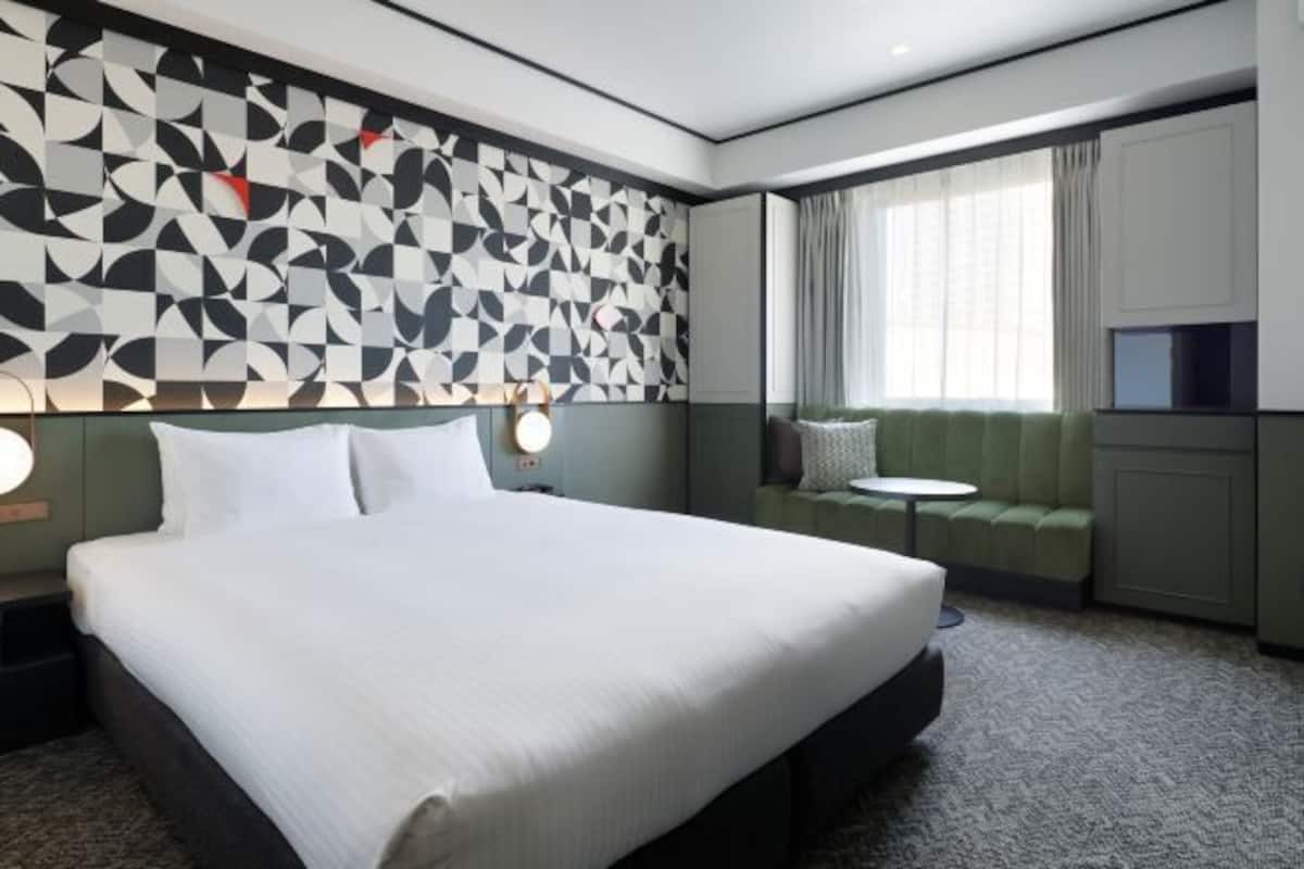 Ett hotellrum med en stor sÀng, en vÀggmonterad TV, en sittgrupp med en grön soffa och ett litet runt bord.