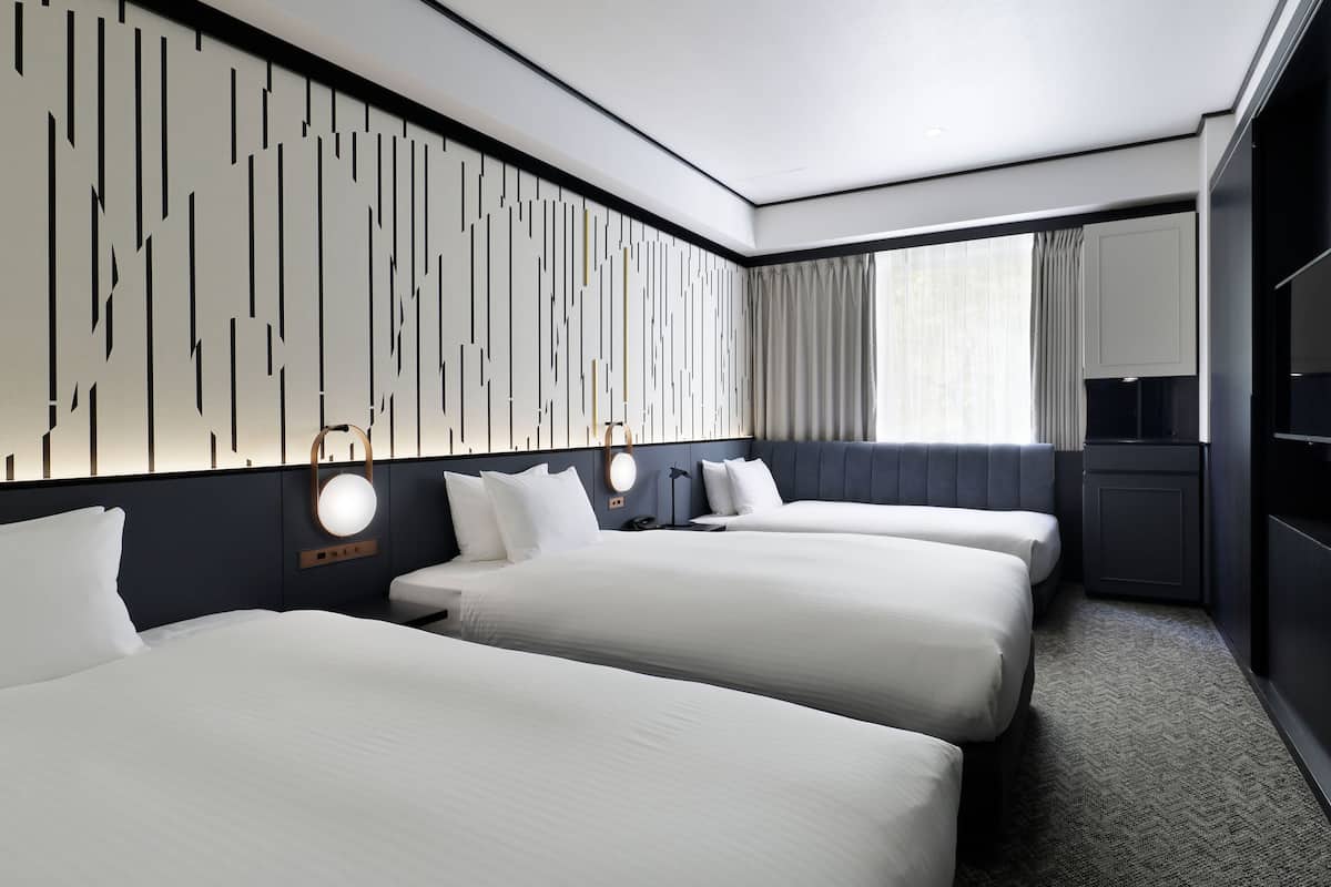 Habitación de hotel con dos camas, un escritorio, un espejo y una pared con diseño geométrico.