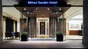 La entrada del Mitsui Garden Hotel, con un diseño moderno, presenta un frente de vidrio, una zona de recepción y un candelabro.