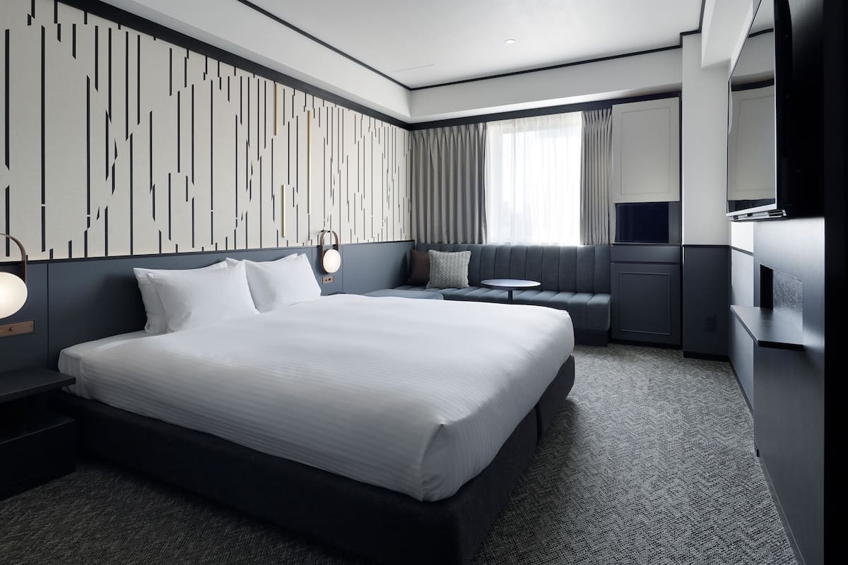 Una habitación de hotel moderna con una cama grande, un área de descanso, una mesita y un televisor.