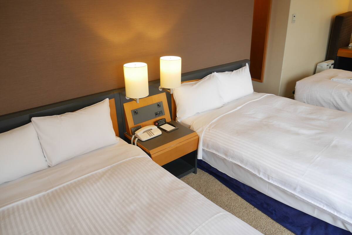 Ein Hotelzimmer mit zwei Betten, einem Nachttisch aus Holz mit Telefon und Lampen sowie einem an der Wand befestigten Spiegel.
