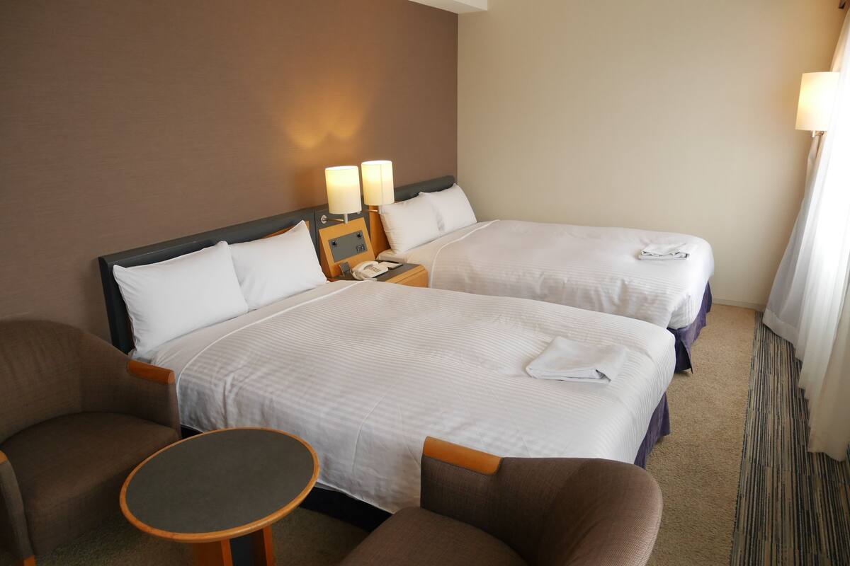 Ein Hotelzimmer mit zwei Betten, einem kleinen Tisch und zwei Sesseln.