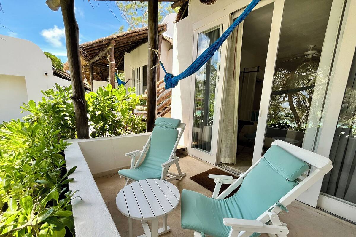 A balcony with two white lounge chairs and a small round table, surrounded by greenery.