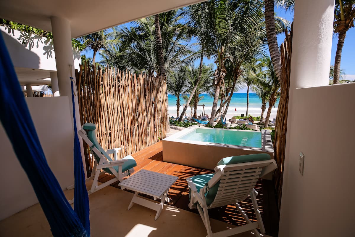 A balcony with a pool, white lounge chairs, and a view of the beach and ocean.