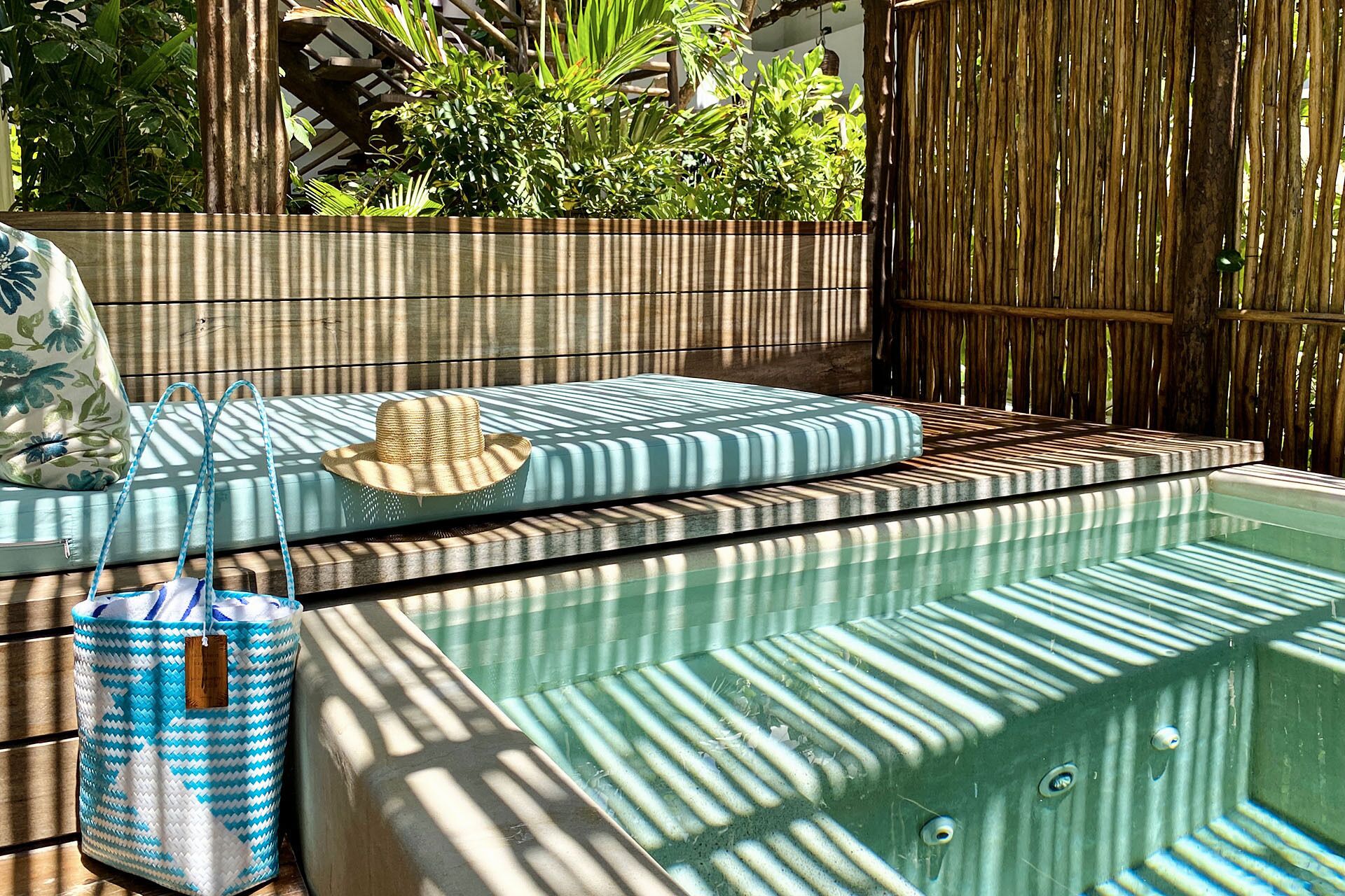 A pool area with a wooden deck, a lounge chair, a hat, and a striped bag.