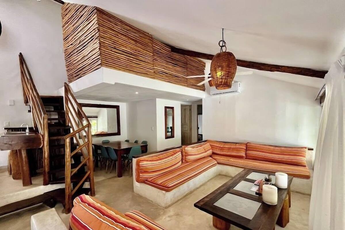 A modern living room with a wooden staircase, a large sectional sofa, and a dining area.