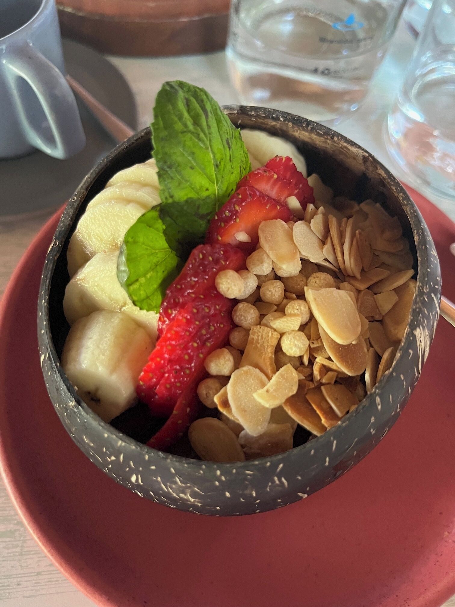 A dessert in a bowl with strawberries, bananas, almonds, and mint leaves.