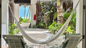 Una hamaca entre dos sillas de descanso con vistas a un jardín tropical y el océano.