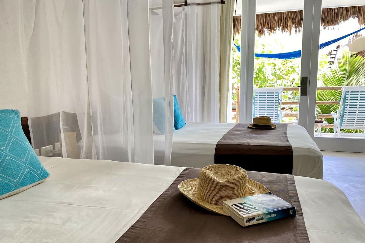 A room with two beds, a straw hat, and a book on one bed.