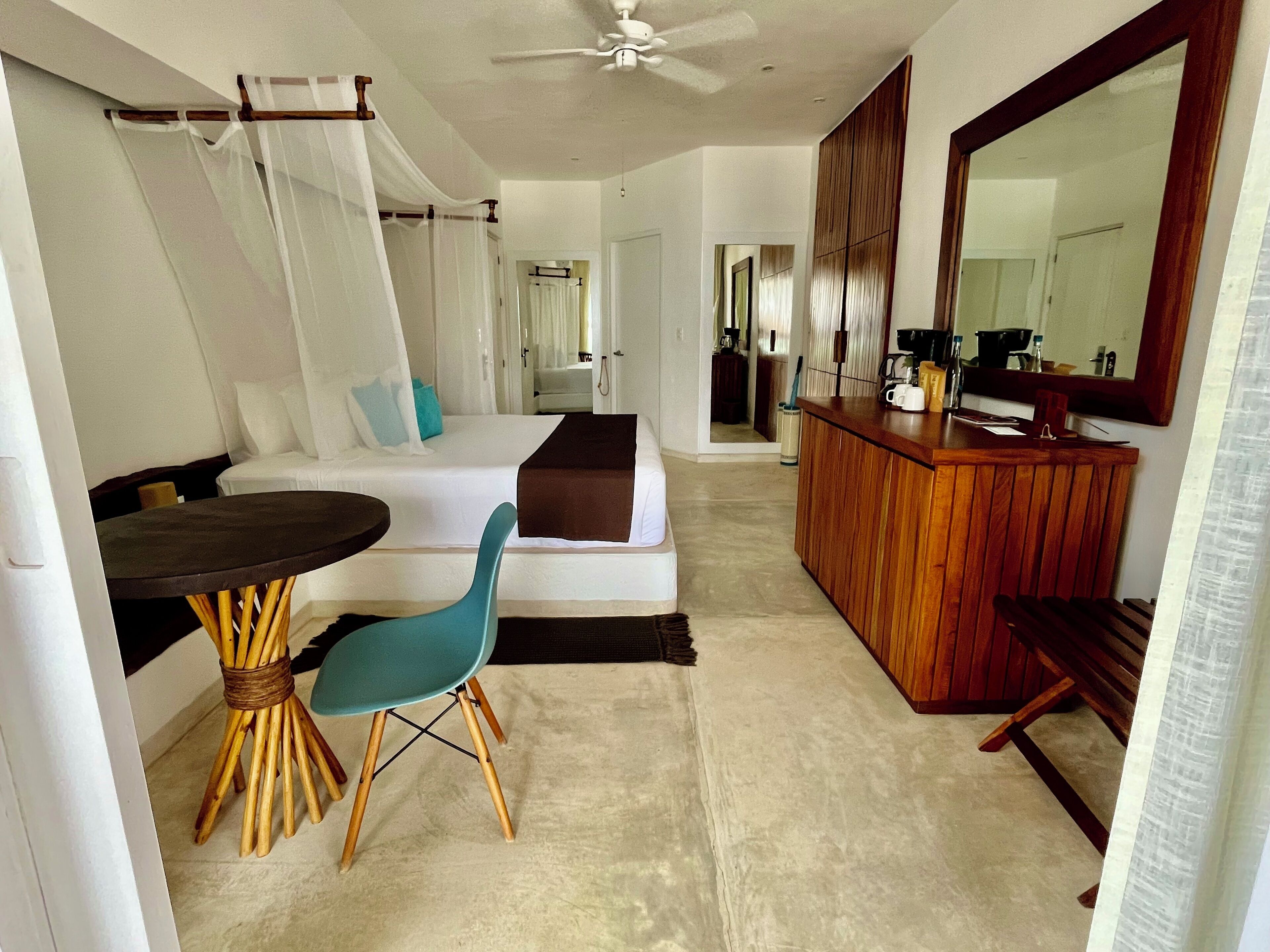 A modern bedroom with a bed, a wooden desk, a chair, a large mirror, and a ceiling fan.