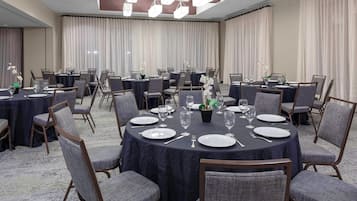 A conference room with round tables, chairs, and a potted plant.