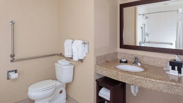 A bathroom with a toilet, grab bar, towel rack, sink, mirror, and a shower area.