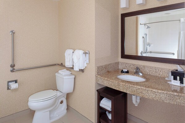 A bathroom with a toilet, grab bar, towel rack, sink, mirror, and a shower area.