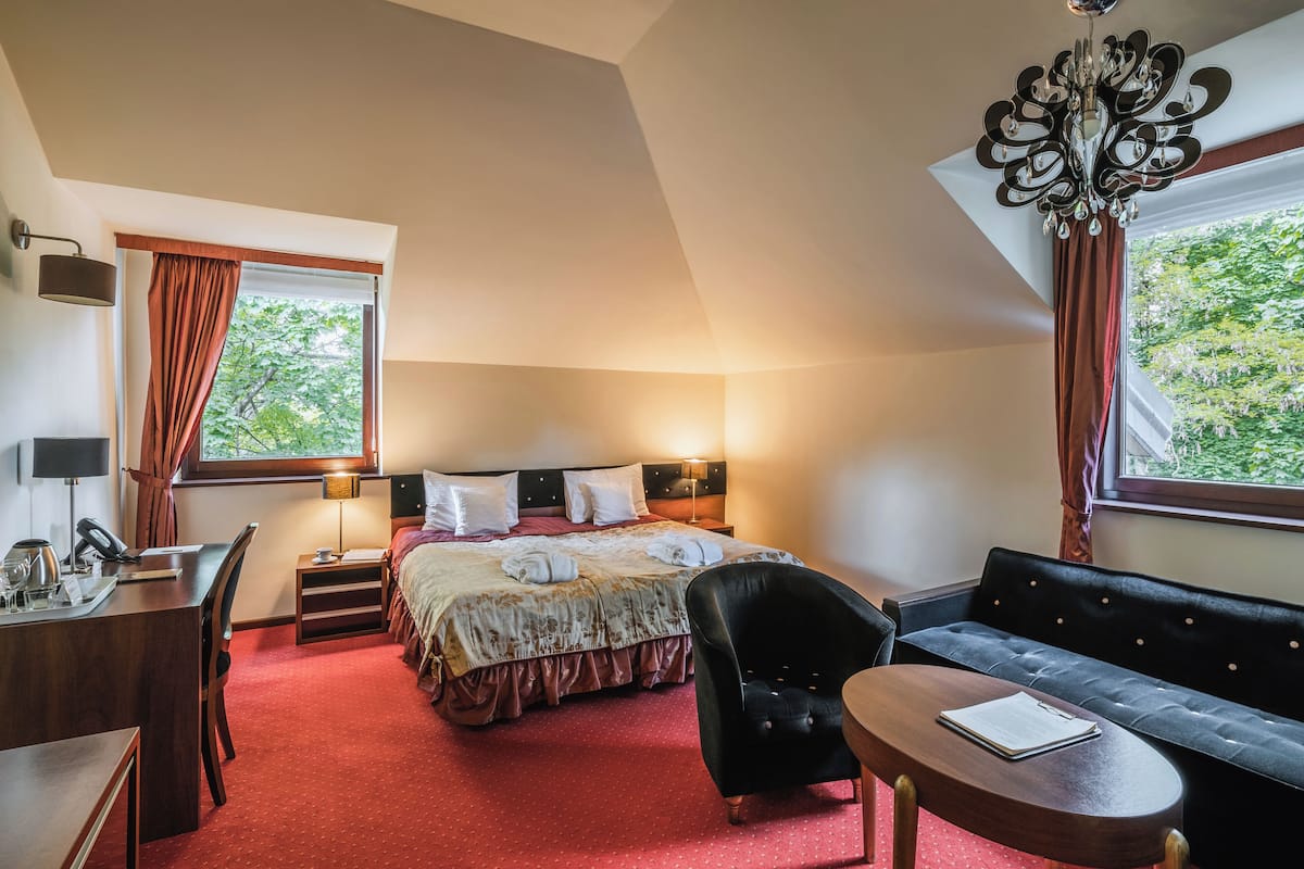 Une chambre d’hôtel avec un lit, un bureau, une chaise, un canapé et un lustre.