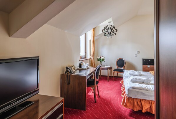 A hotel room with a TV, desk, chair, bed, and a small table with a plant.