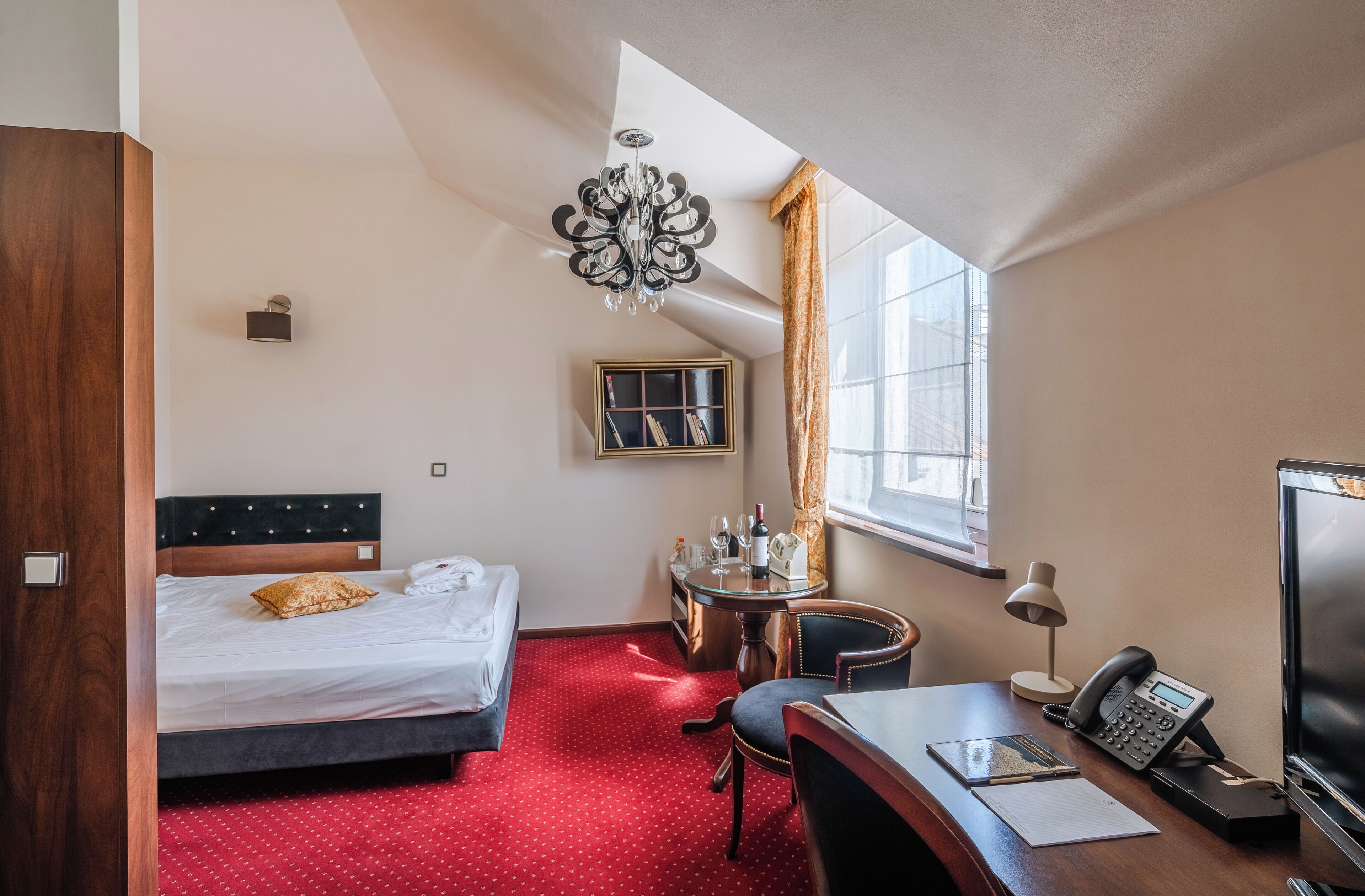 Une chambre d’hôtel avec un lit, un bureau, une chaise et une petite table avec une lampe.