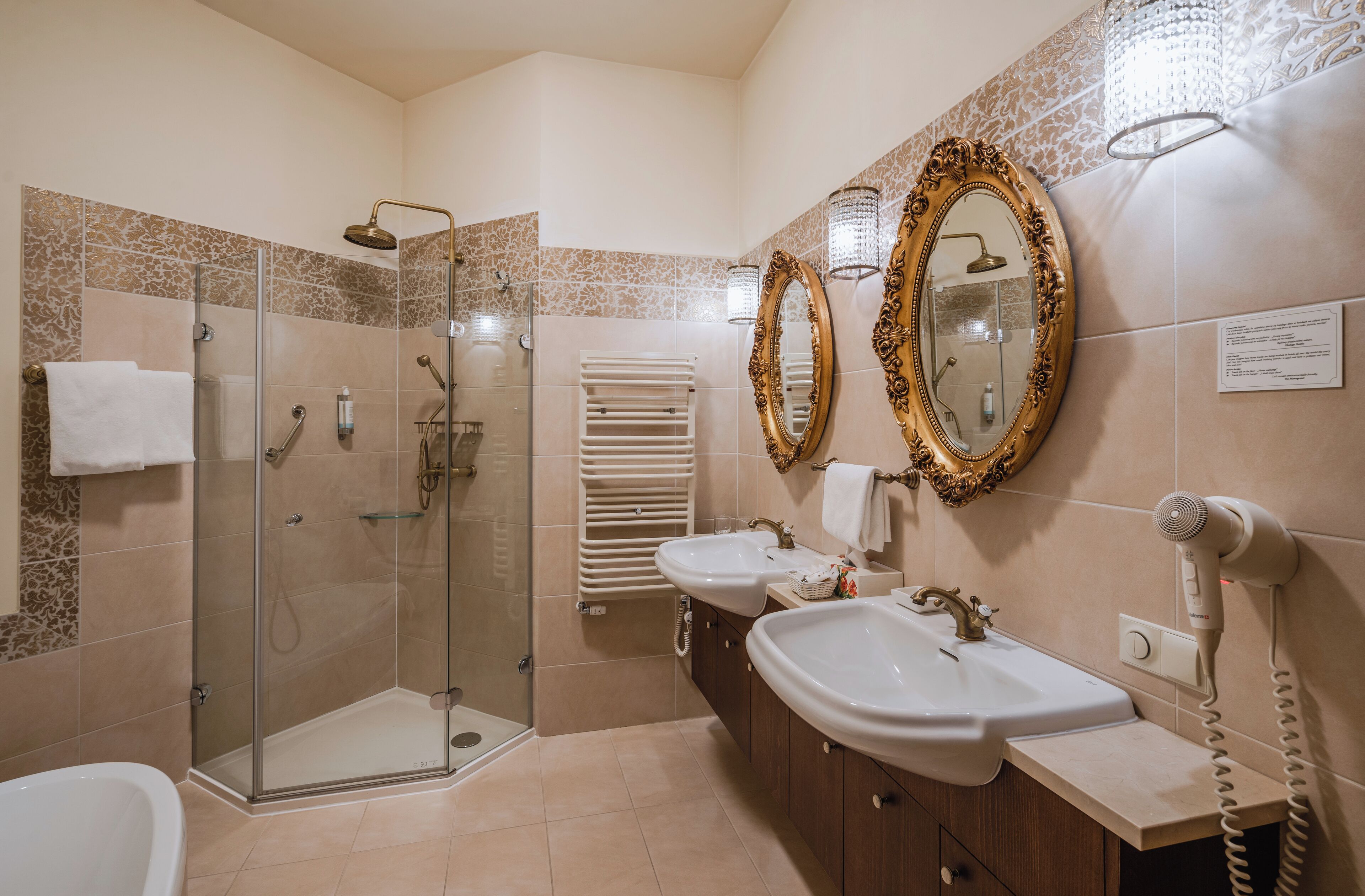 A bathroom with a glass shower enclosure, two sinks, a vanity, and a hairdryer.