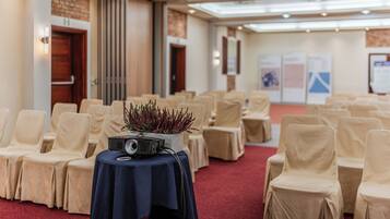 A conference room with rows of beige chairs, a table with a projector, and a red carpet.