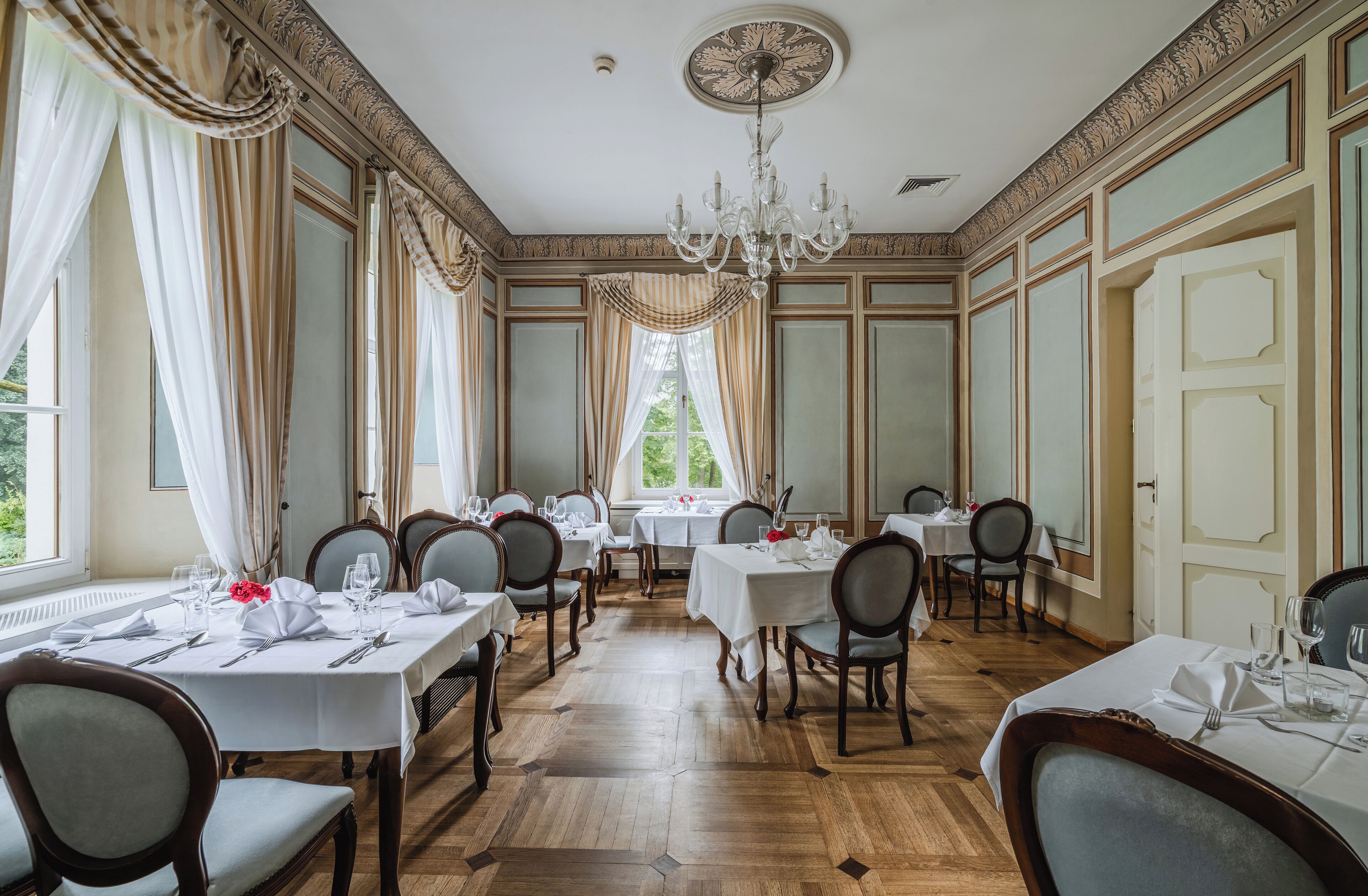 A formal dining room with multiple tables, elegant chandeliers, and classic decor.
