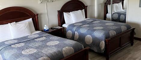 A hotel room with two wooden beds, a ceiling fan, and a large mirror.