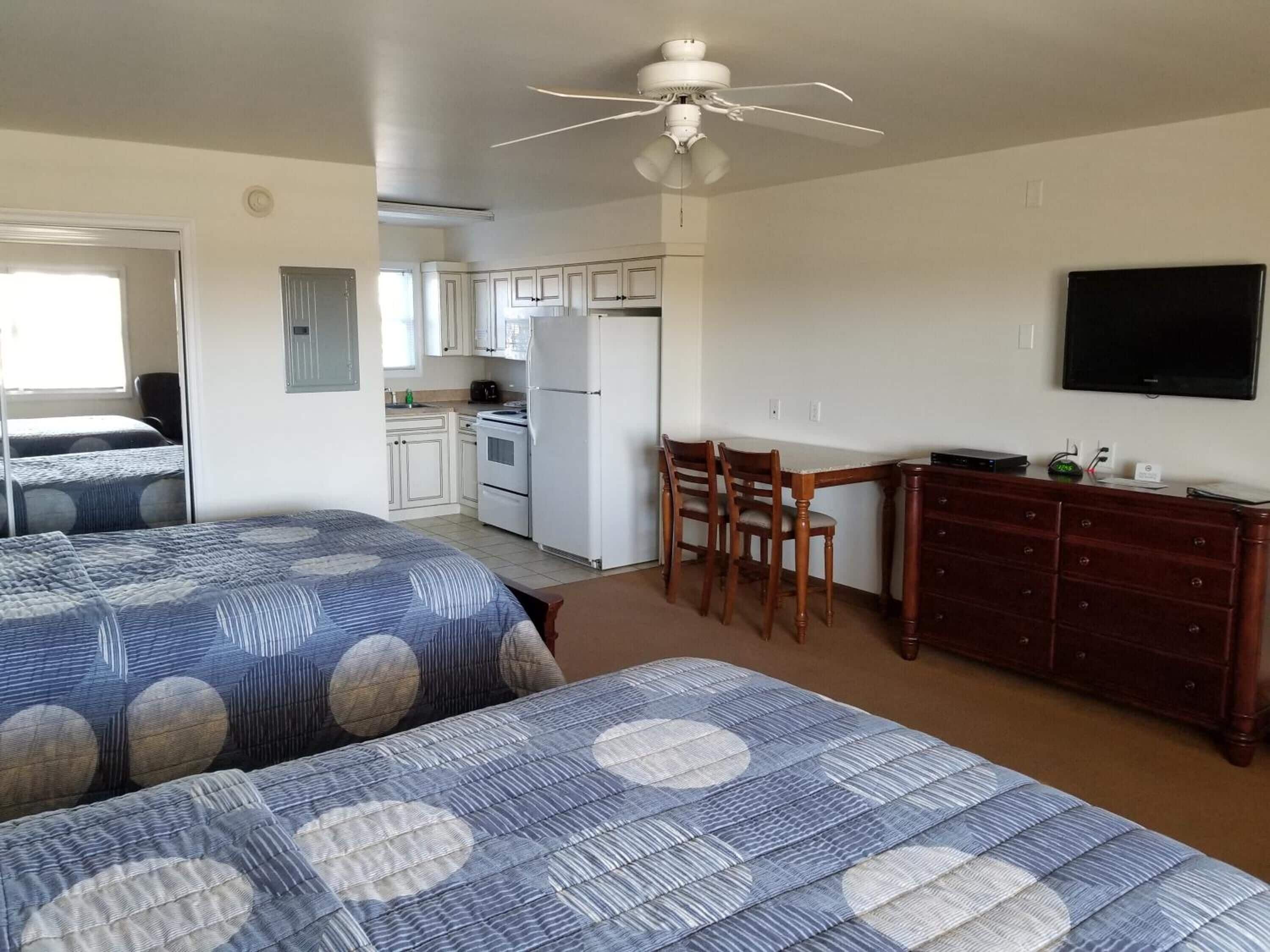 A room with two beds, a kitchenette, a dining area, and a TV.