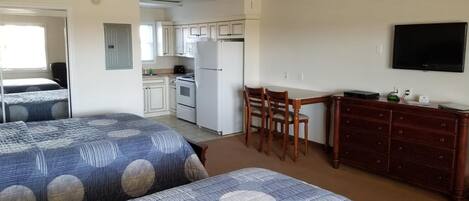 A room with two beds, a kitchenette, a dining area, and a TV.