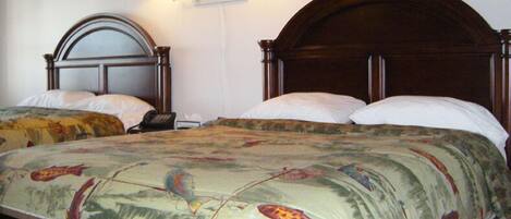 A hotel room with two wooden beds, each with a headboard and white bedding. There are wall-mounted lamps on either side of the beds.