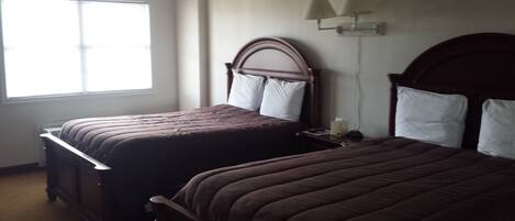 Quarto de hotel com duas camas, uma mesa de cabeceira, um abajur e uma janela.
