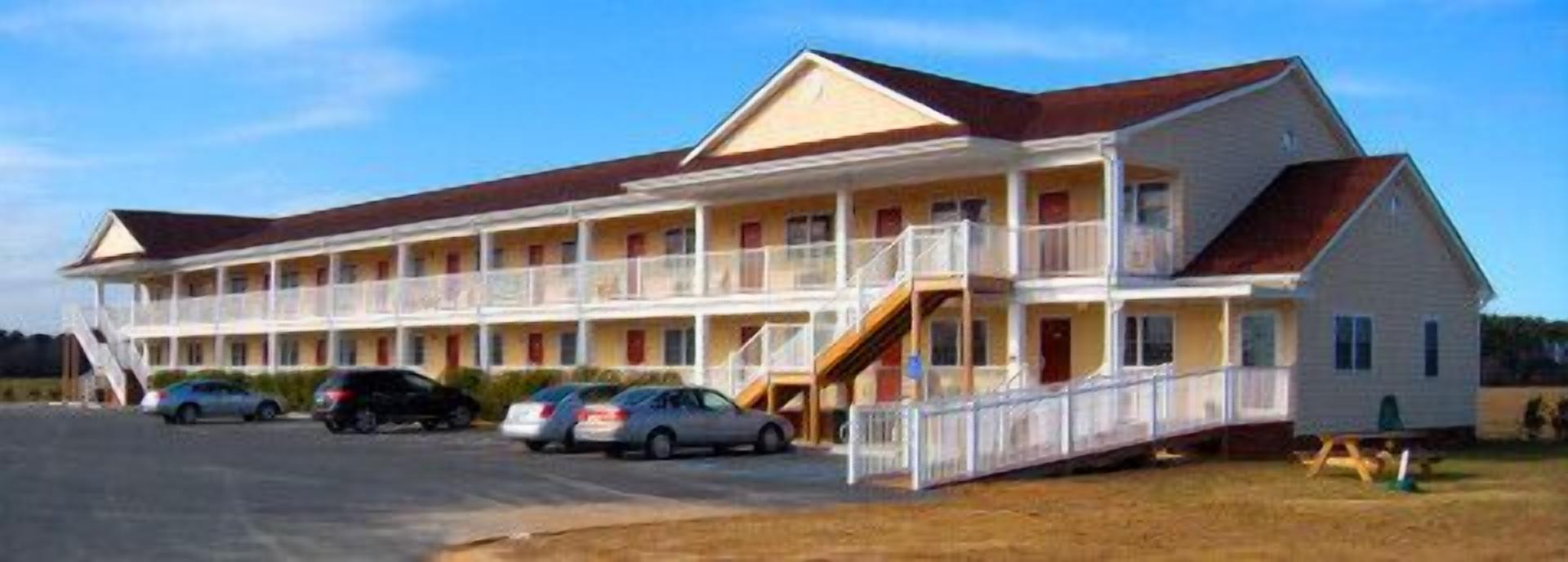Un motel con estructura de dos pisos, varios balcones y zona de estacionamiento techada.