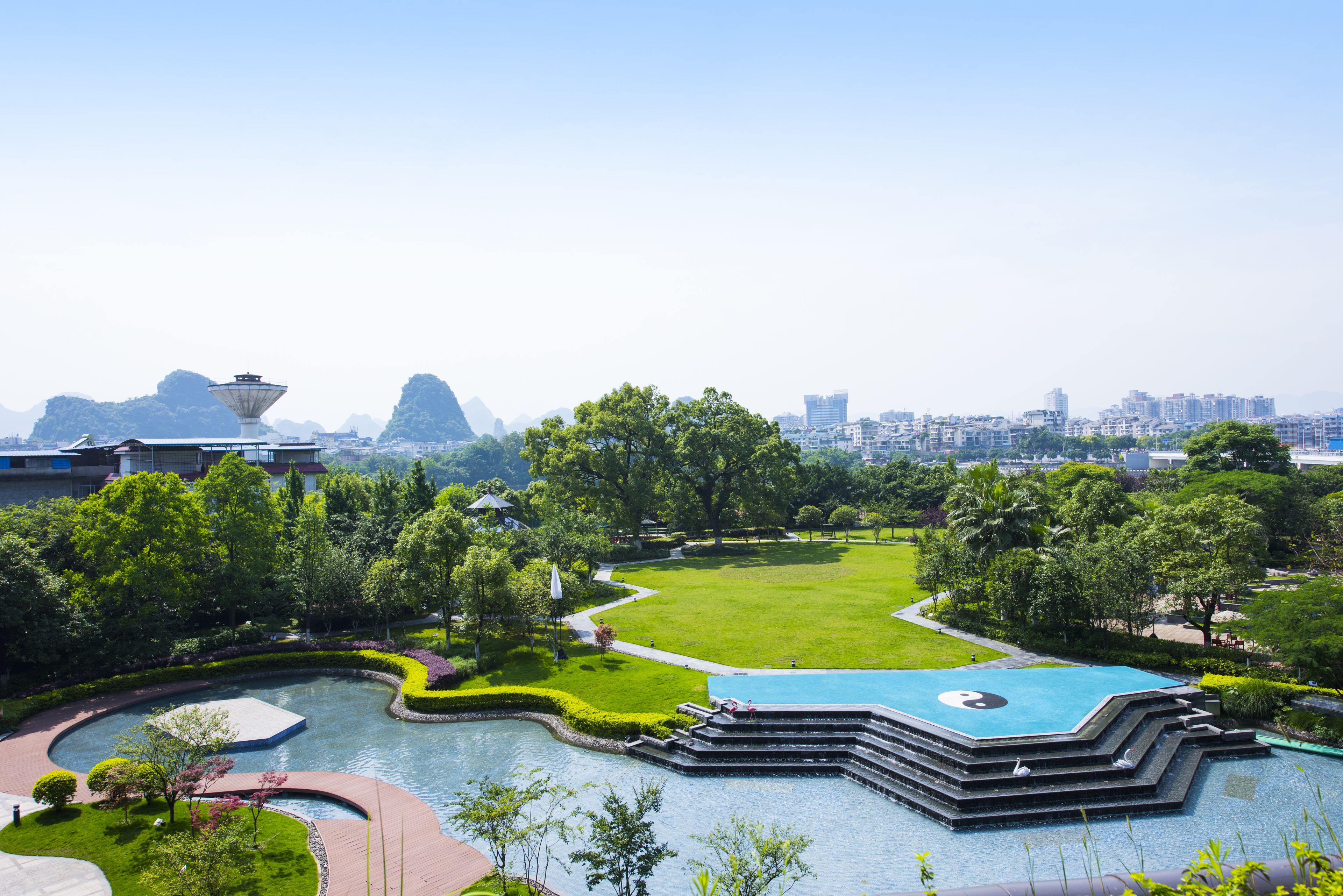 A landscaped area with a pool, pathways, and a view of a cityscape in the background.