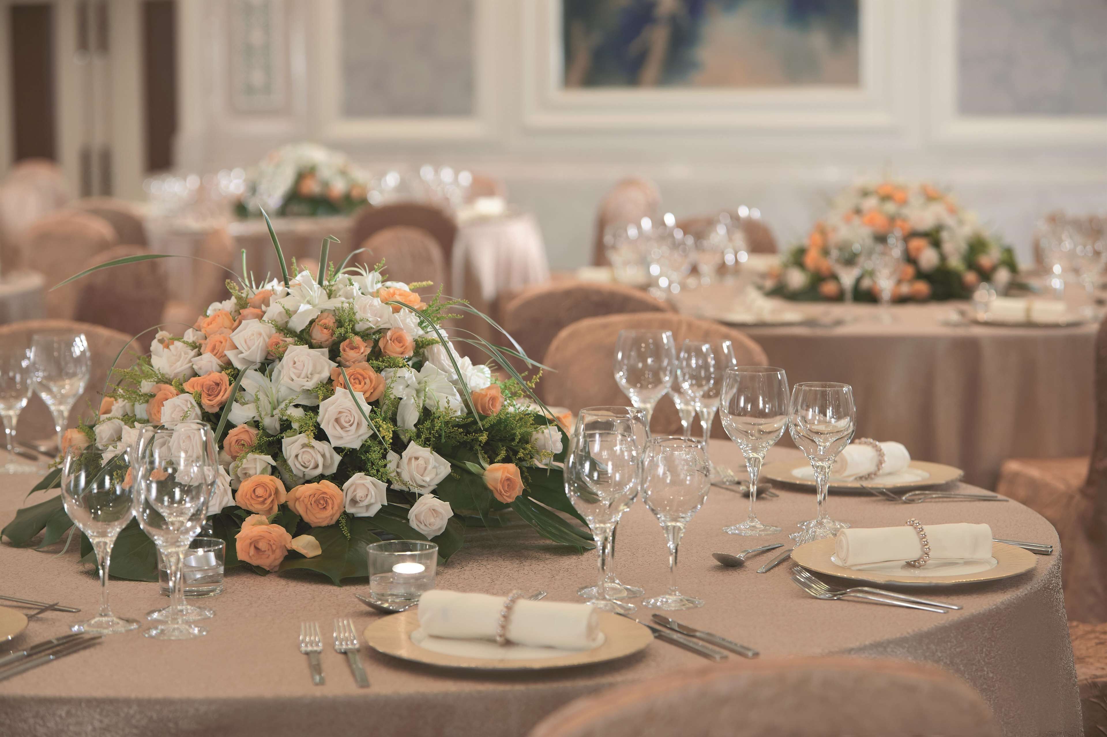 A banquet hall with round tables set for a formal event, featuring floral centerpieces and neatly arranged tableware.