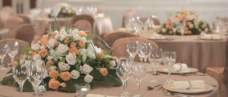 Une salle de banquet avec des tables rondes dressées pour un événement formel, agrémentée de compositions florales et d’une vaisselle soigneusement disposée.