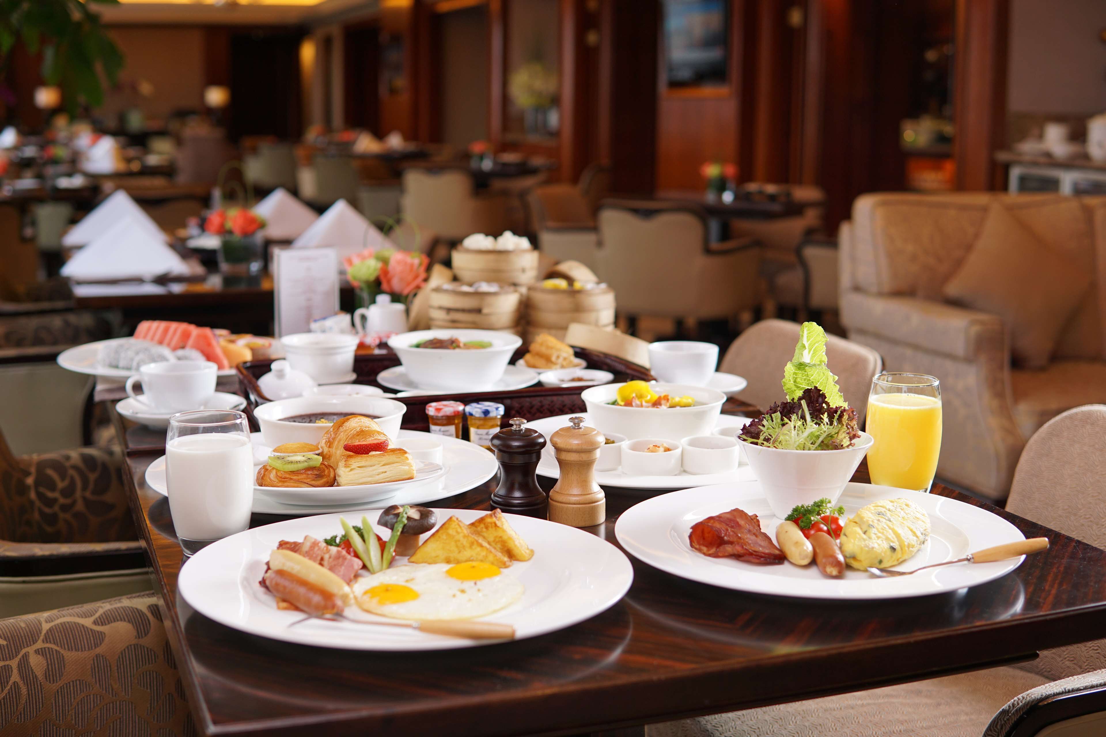 A breakfast buffet with various dishes, including eggs, bacon, and toast, on a wooden table in a hotel dining area.