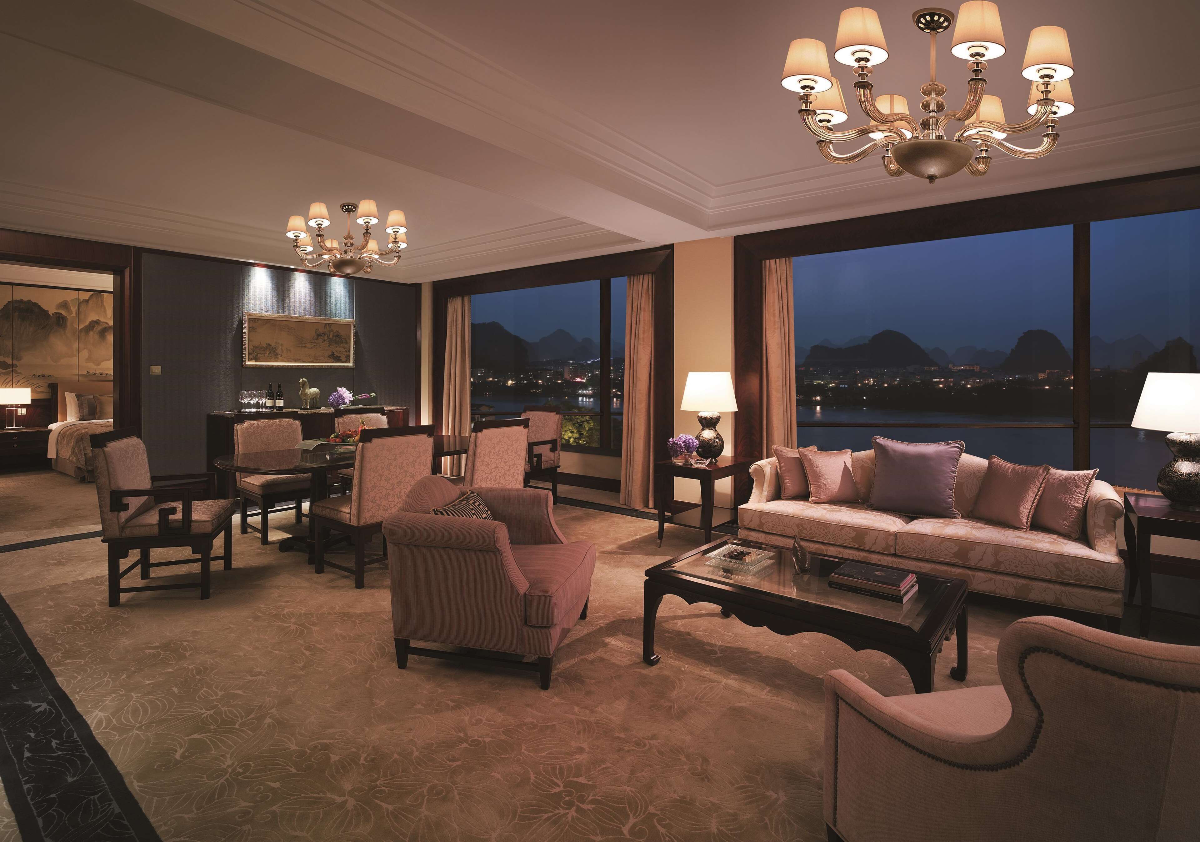 A spacious living room with a large window offering a view of the cityscape and mountains at dusk.