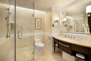 Un baño moderno con ducha de vidrio, inodoro, lavamanos con tocador y un espejo grande.
