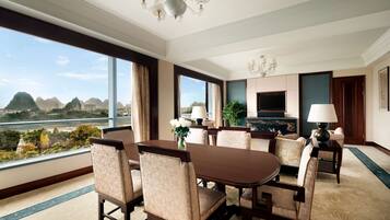 Habitación de hotel con zona de comedor, ventanas amplias con vista a las montañas, un candelabro y un televisor de pantalla plana.