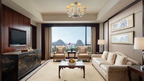 Habitación de hotel con un ventanal grande, un televisor de pantalla plana, un sofá, una mesa de centro y un aparador decorativo.