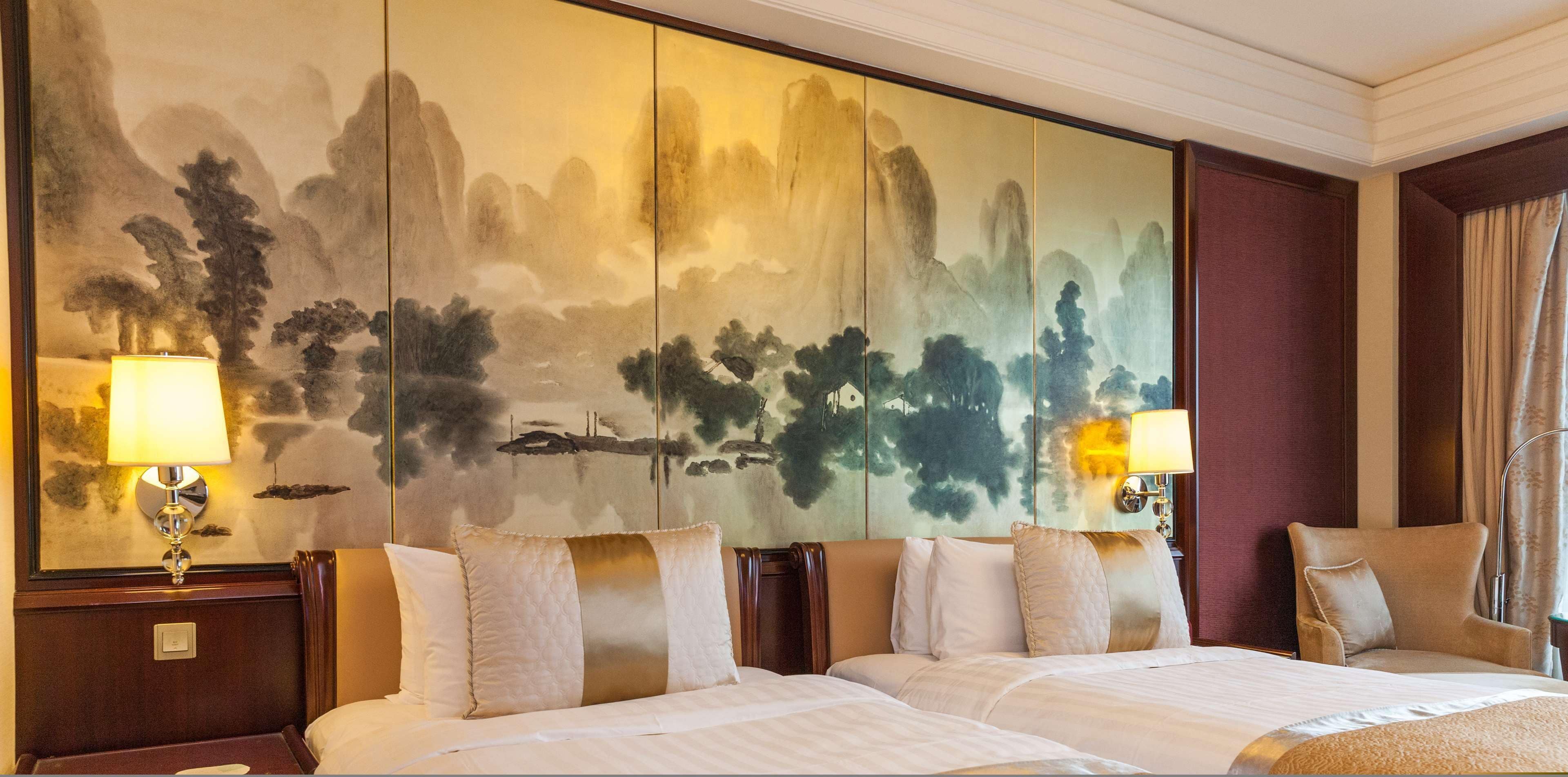 A hotel room with a large wall painting, two bedside lamps, and a bed with multiple pillows.