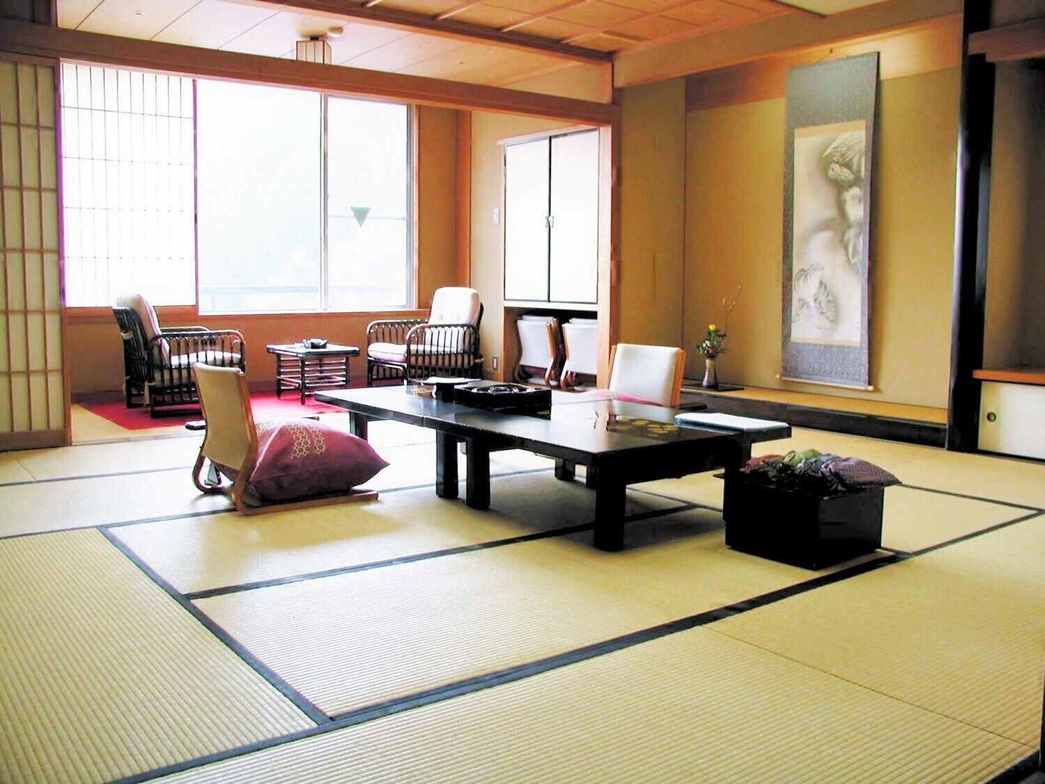 Une pièce avec un sol recouvert de tatamis, une petite table, des chaises et un tableau accroché au mur.
