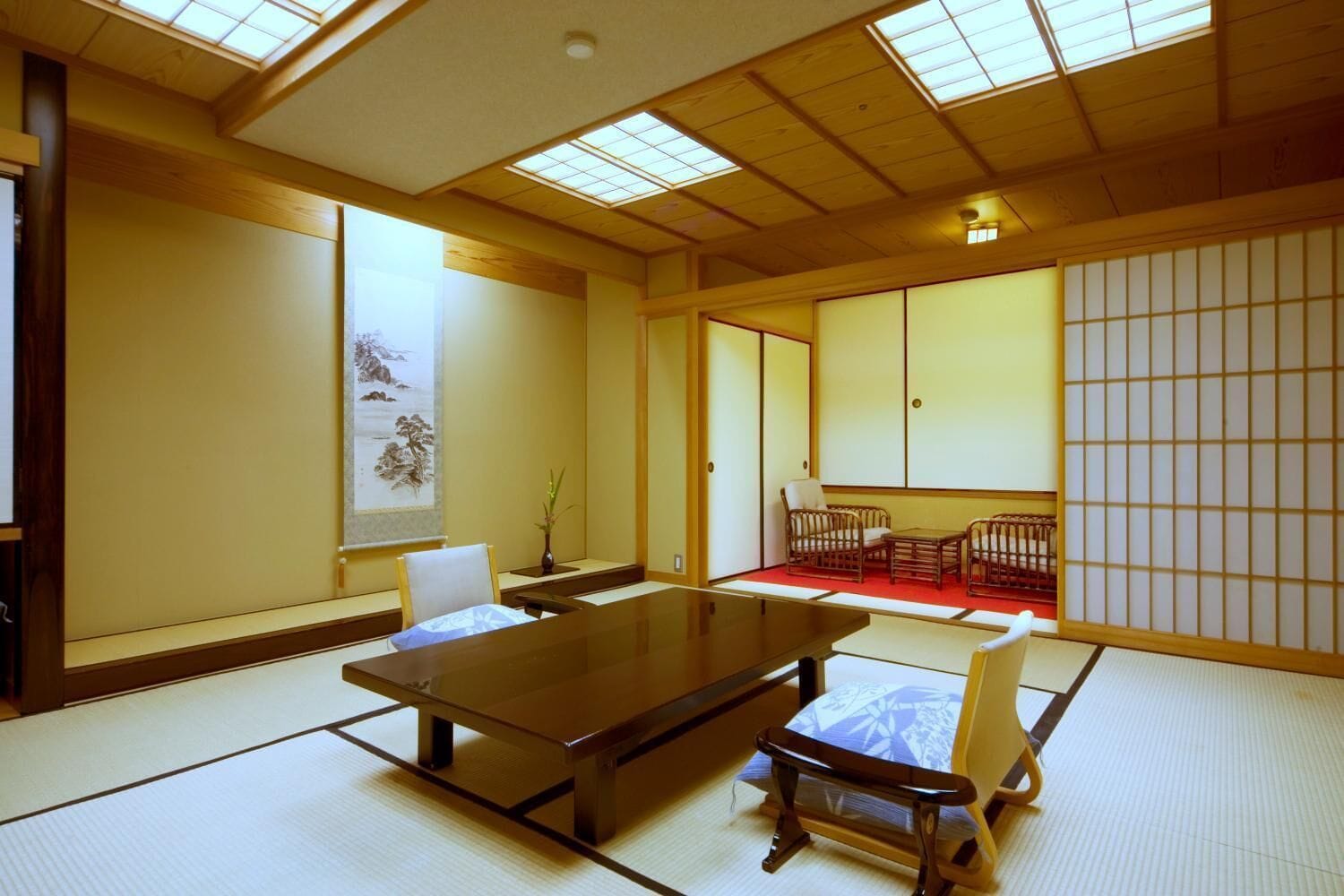 A traditional Japanese room with tatami flooring, a low table, and a seating area with cushions and a low table.